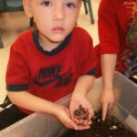 Children holding soil over a bin the classroom