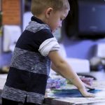 young boy painting with hands