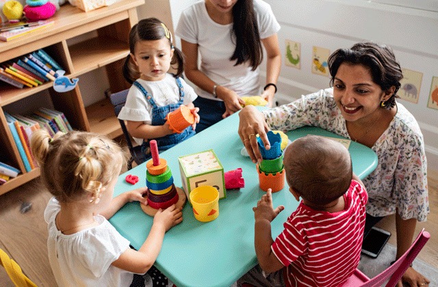 Toddlers and teachers play with blocks around a table